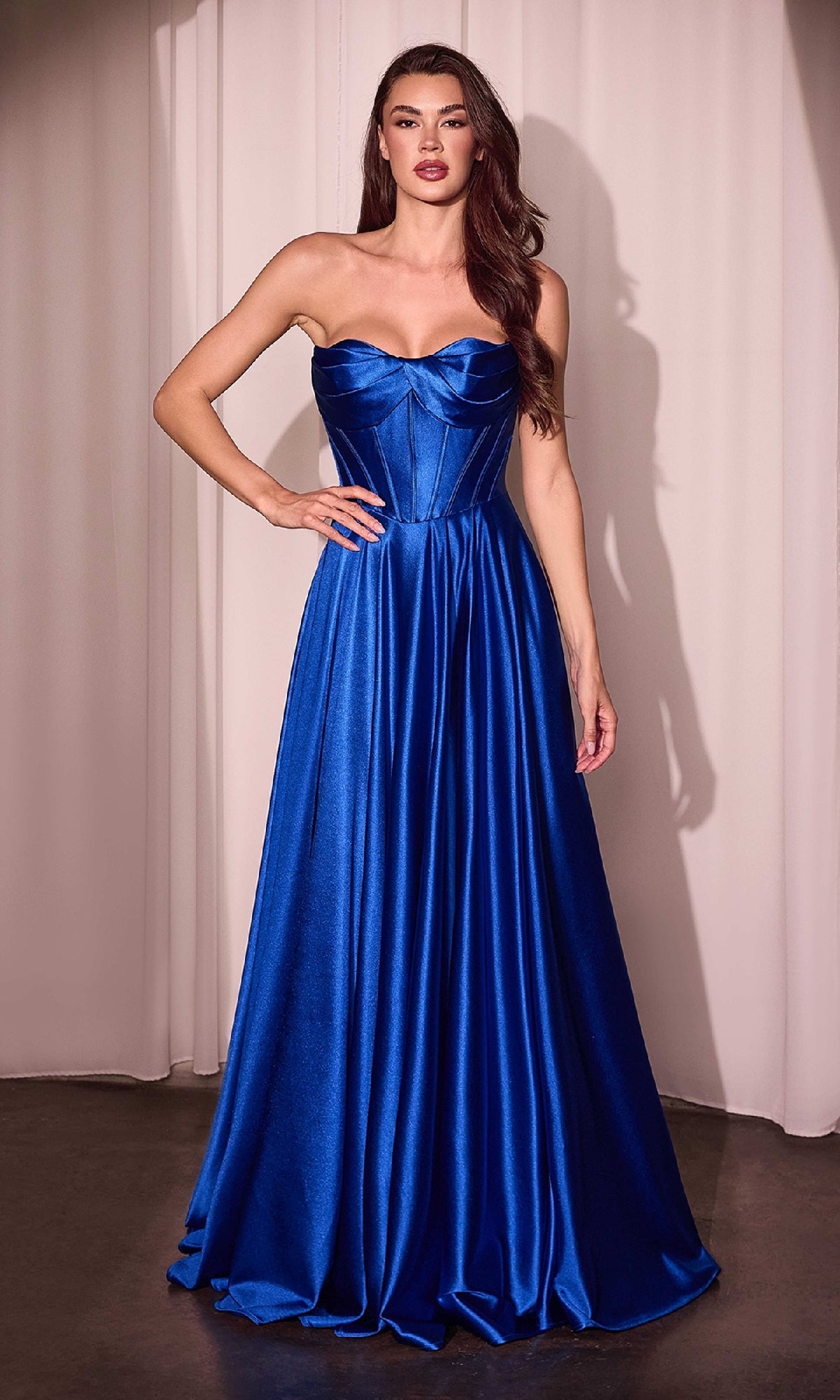 A woman stands before a curtain wearing the Ladivine CD378 Strapless Long A-Line Prom Dress, featuring royal blue satin, a fitted corset-style bodice, and a flowing floor-length skirt.